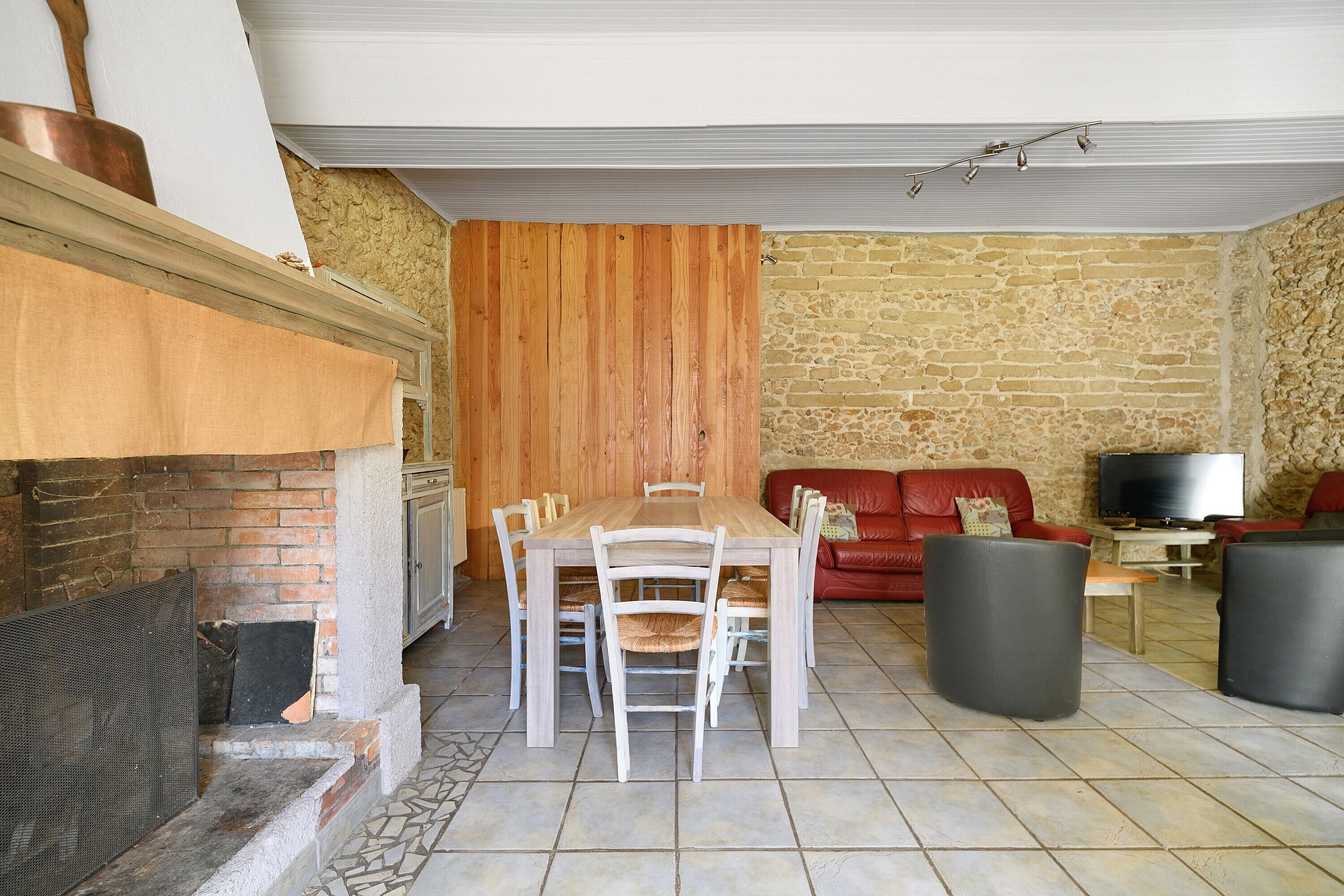 A dining area with a wooden table and chairs, a fireplace, a stone wall, and a red sofa.