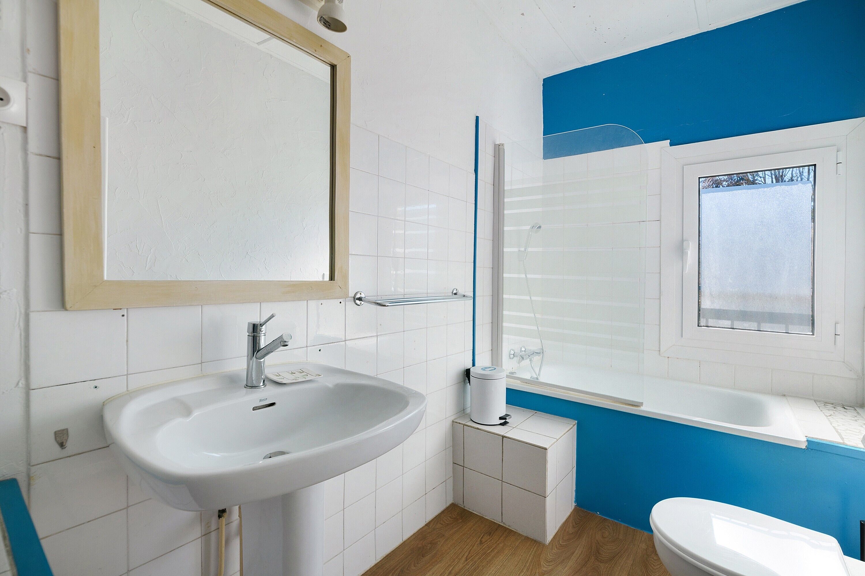 A bathroom with a sink, mirror, window, and bathtub.