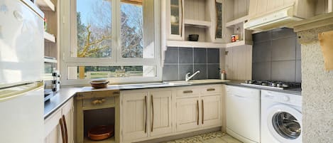 Een keuken met een raam, een wasmachine en een betegelde vloer.