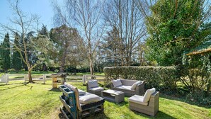 An outdoor seating area with wicker furniture and a wooden table, surrounded by a well-maintained lawn and trees. - Gîte de Marlas - Ariège (Rieucros)