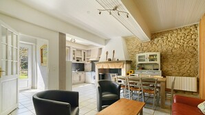 A spacious living area with a dining table, chairs, a sofa, and a kitchen in the background. - Gîte de Marlas - Ariège (Rieucros)