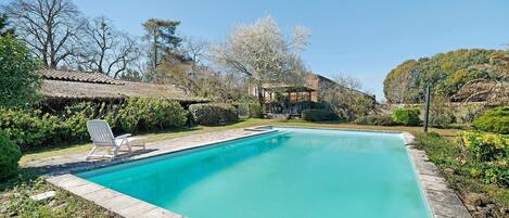 A rectangular swimming pool with a clear blue water, surrounded by a stone border, and a lounge chair.