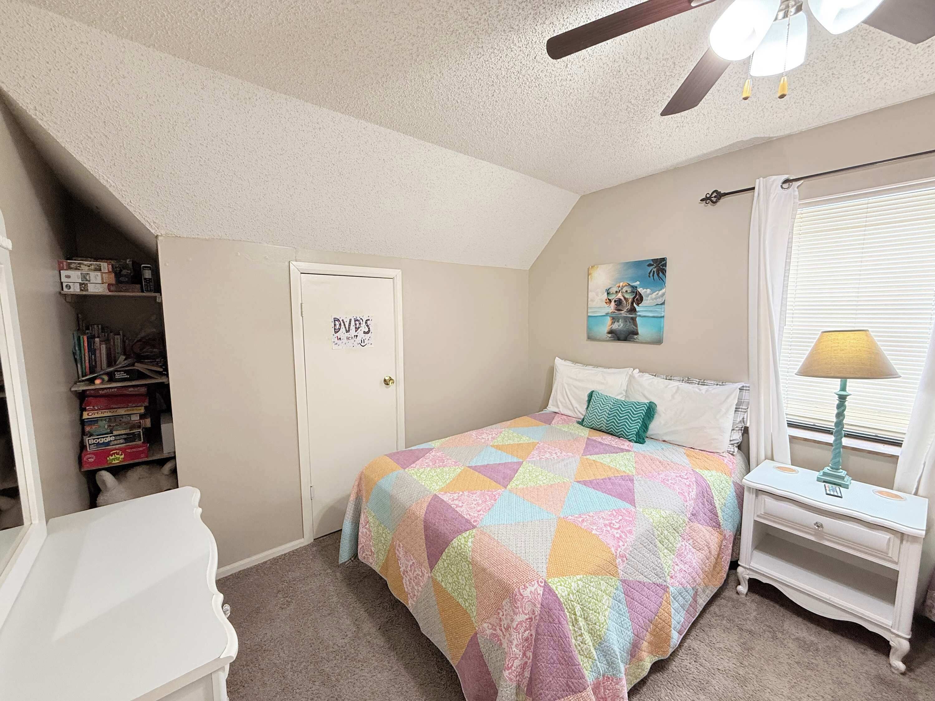 A bedroom with a bed, a nightstand, a bookshelf, a door, and a ceiling fan.