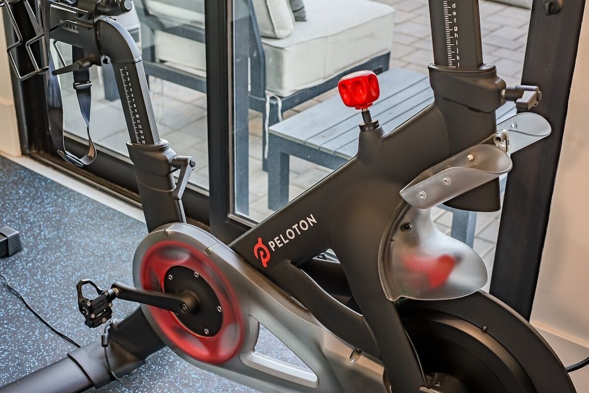 A Peloton stationary bike in a gym with a window view.