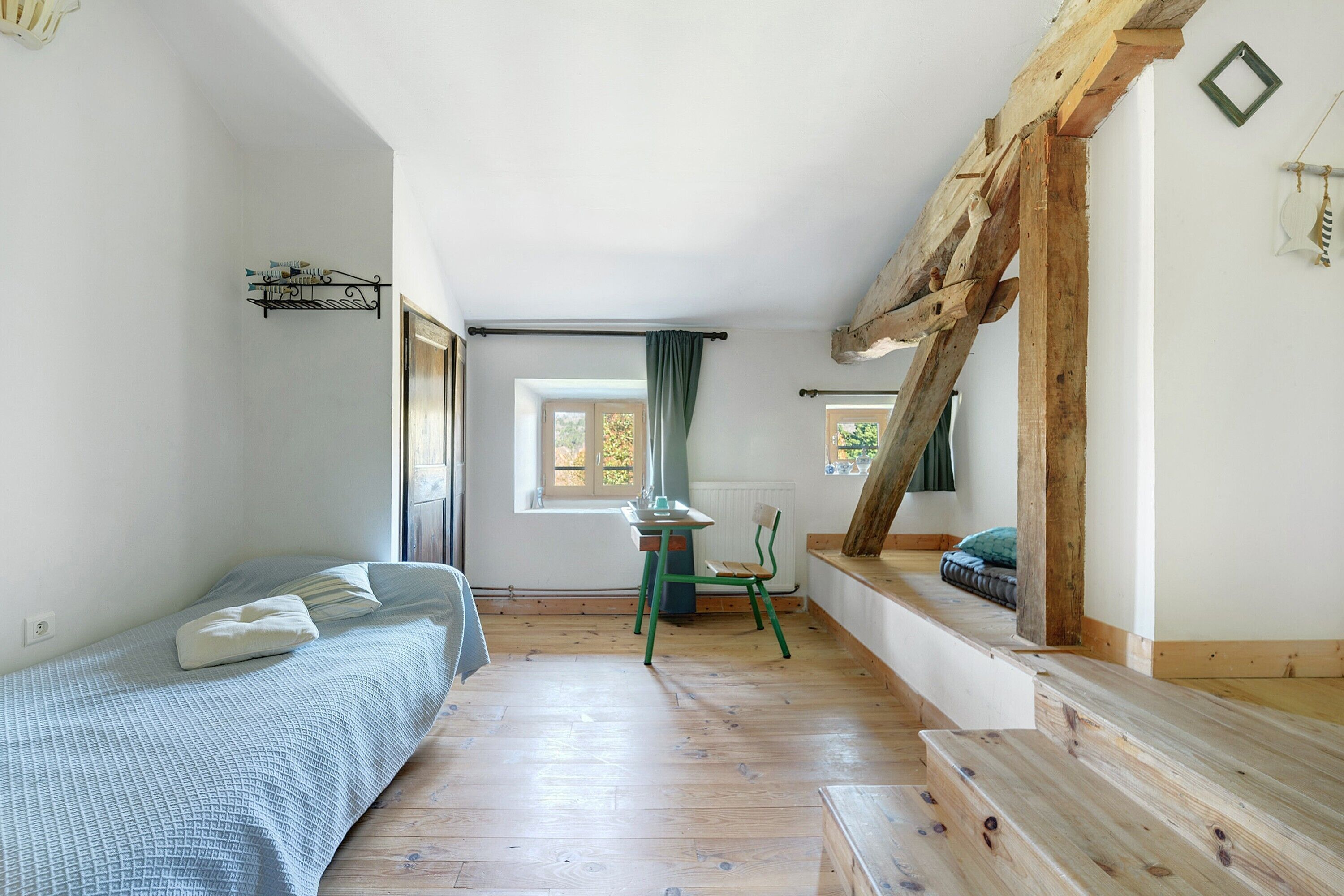 Una habitación con cama, una silla, una mesa y un ventanal.