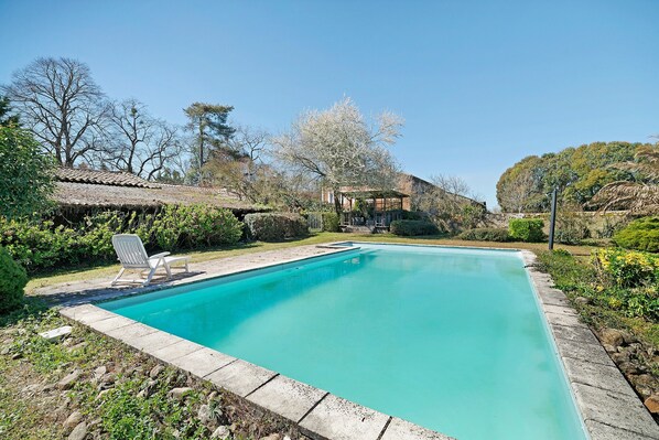 A rectangular swimming pool with a clear blue water, surrounded by a stone border, and a lounge chair.