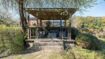 Una pergola in legno con una scalinata che vi conduce, immersa nel verde e delimitata da un muro in pietra.