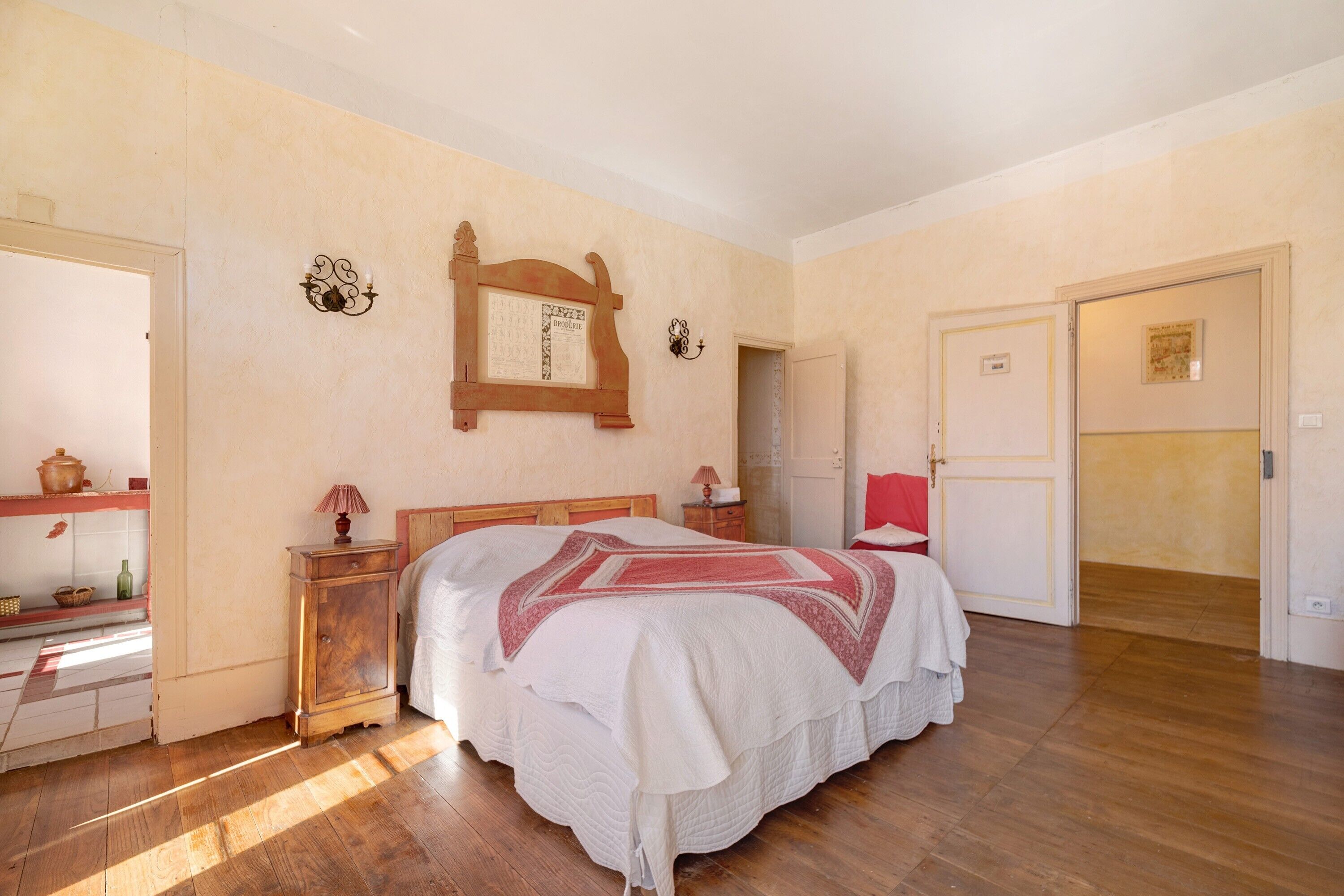 A bedroom with a wooden bed, a nightstand, a mirror, and a door leading to another room.