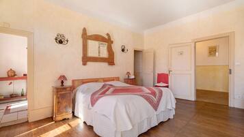 A bedroom with a wooden bed, a nightstand, a mirror, and a door leading to another room.