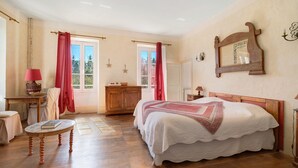 Un dormitorio con una cama, un aparador de madera, una mesa con un libro y una ventana con cortinas.