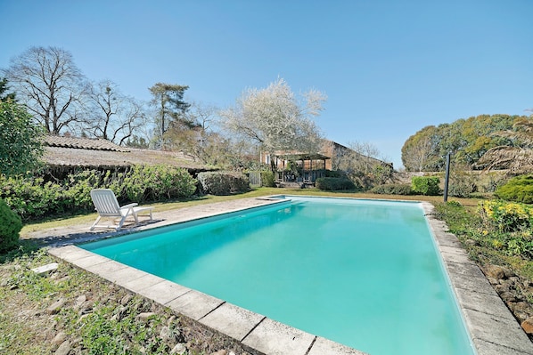 A rectangular swimming pool with a clear blue water, surrounded by a stone border, and a lounge chair.