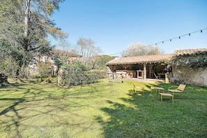 A rustic outdoor seating area with wooden furniture, a pergola, and a stone wall.
