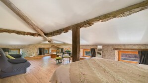 Une chambre spacieuse située dans les combles, avec un grand lit, des poutres apparentes, un canapé et un coin repas offrant une vue agréable.