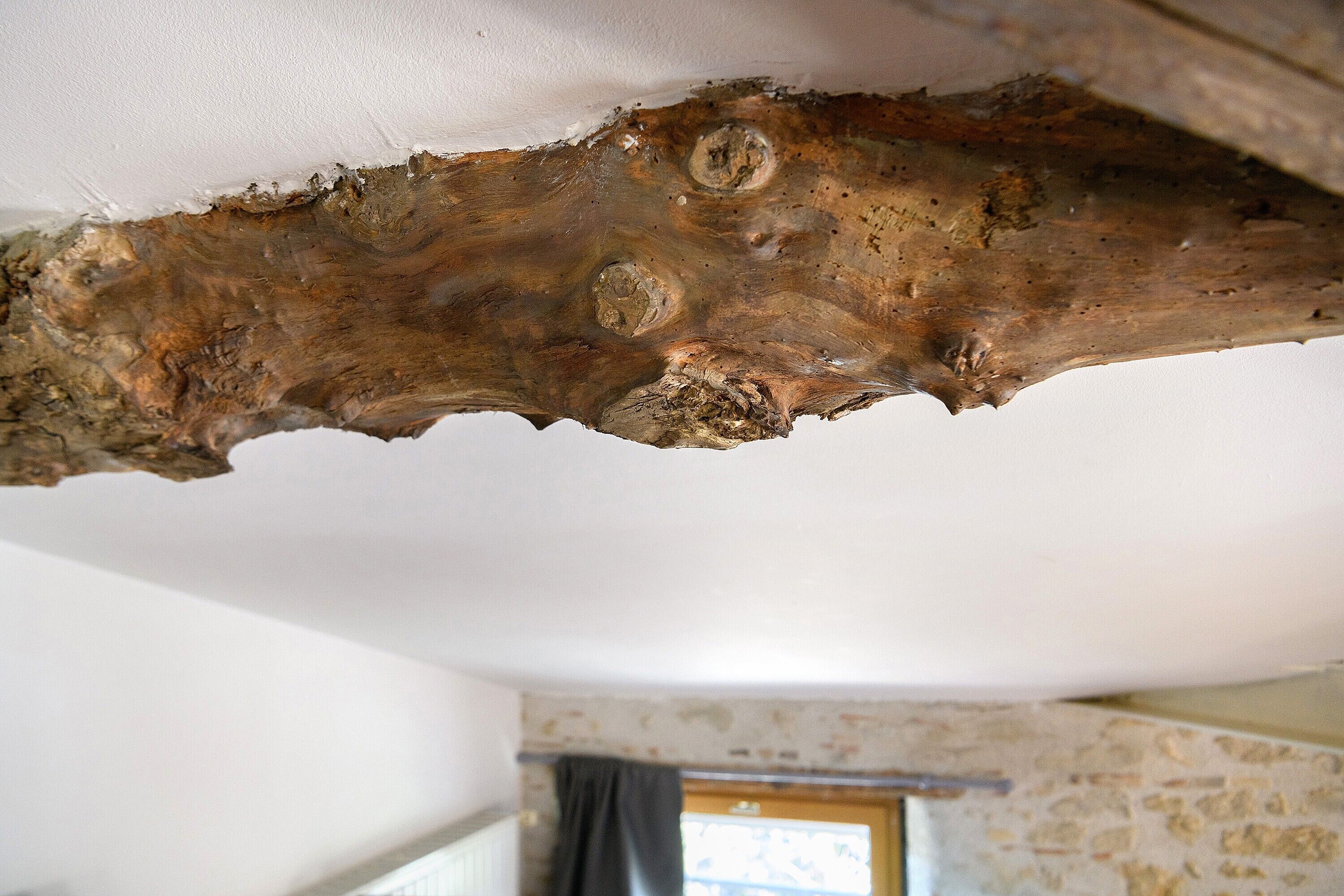 A rustic ceiling with exposed wooden beams and a stone wall.