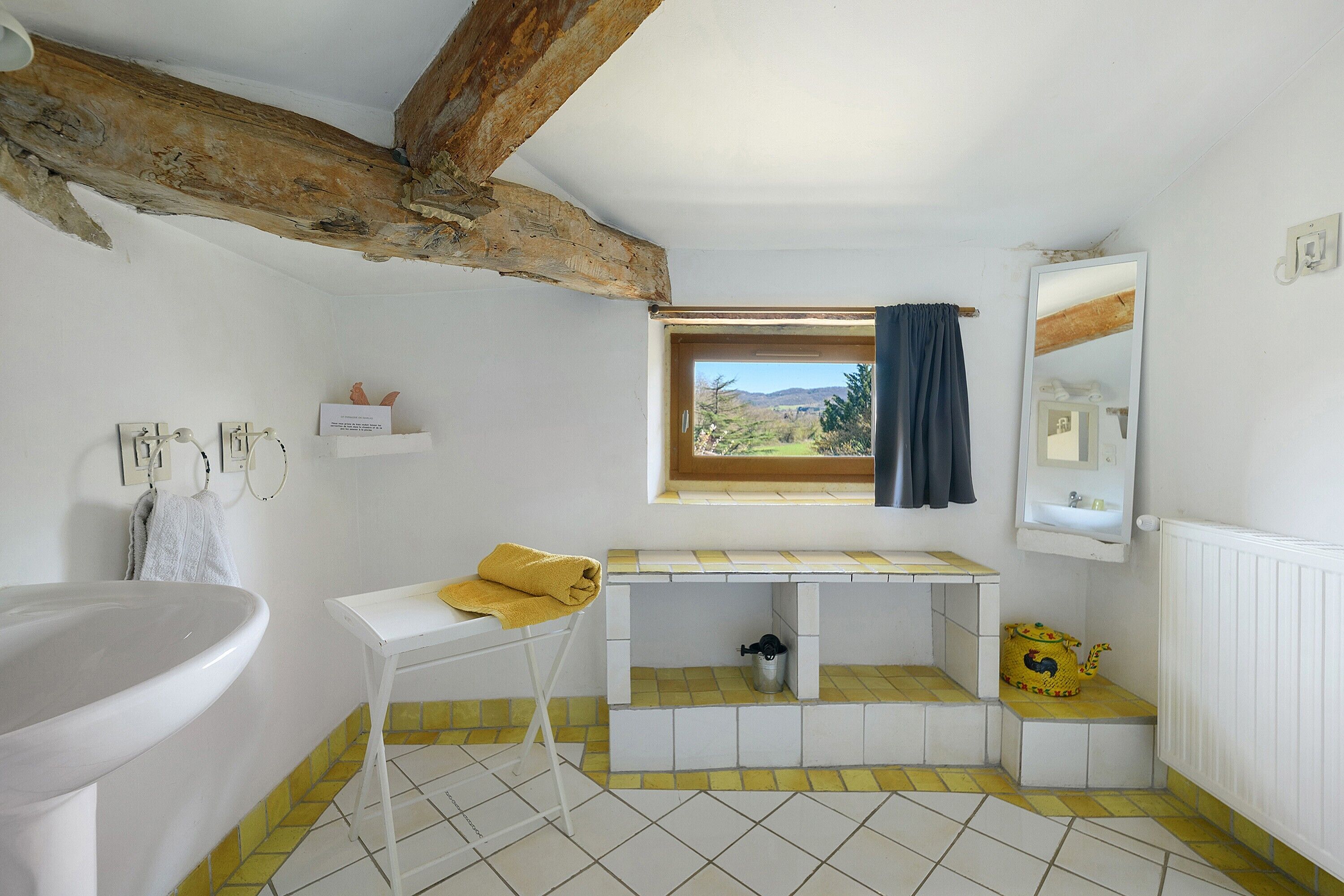 Une salle de bain avec une baignoire, un lavabo, une fenêtre donnant sur un beau paysage et un miroir.