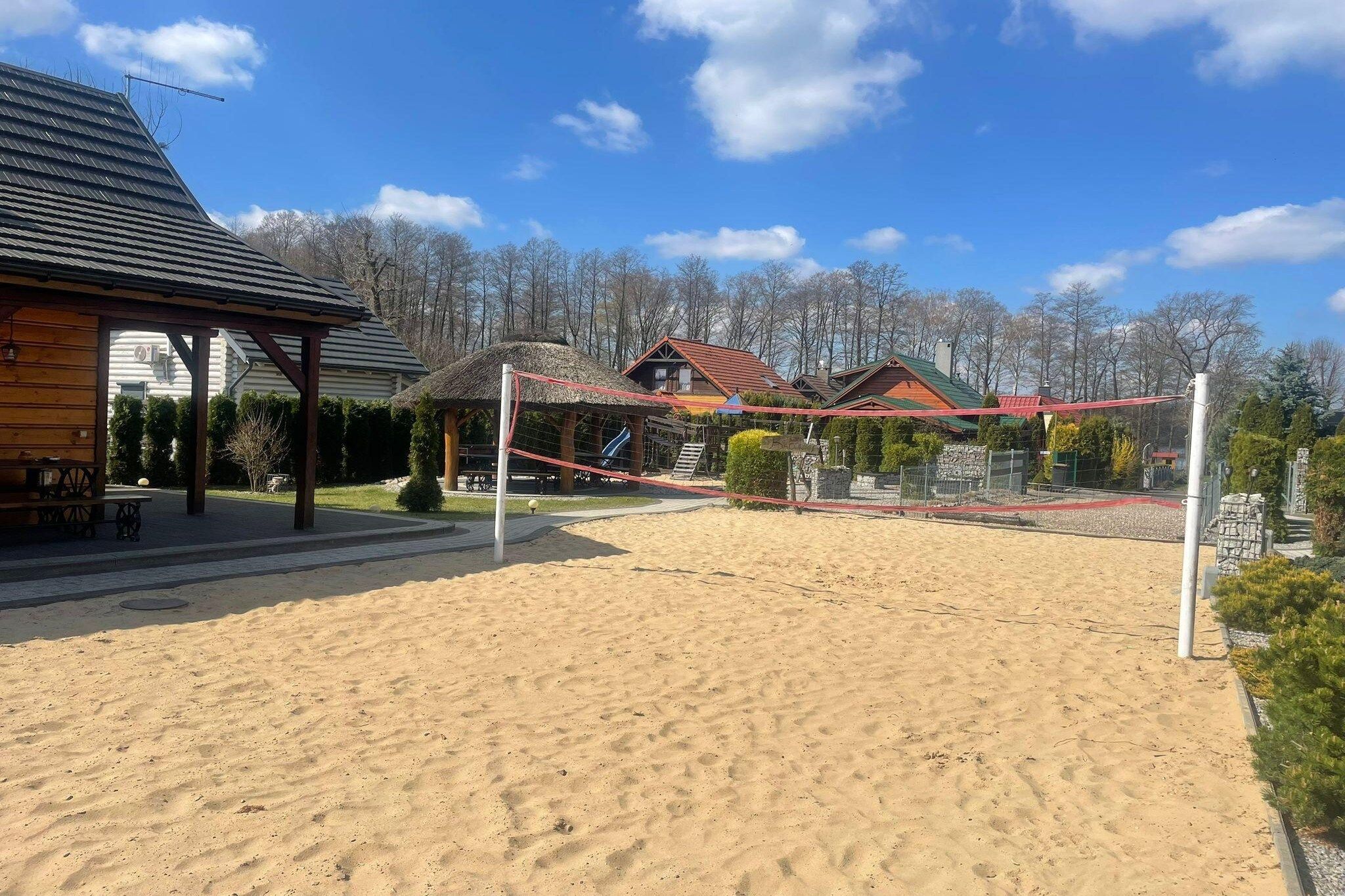 Ein Sandvolleyballfeld mit Netz, umgeben von Holzbauten und Bäumen.