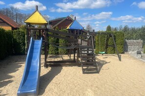 A playground with a blue slide, a yellow climbing structure, and a wooden playhouse.