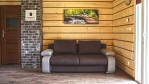 A wooden cabin interior with a brown sofa, a brick fireplace, and a framed picture of a stream. - Holiday homes with fireplaces, playground (Lubrza)