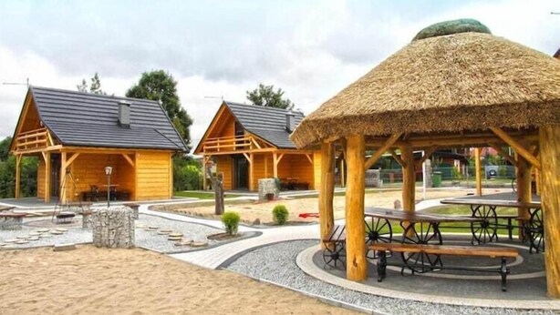 A wooden cabin with a thatched roof, a stone fireplace, and a picnic table with benches. - Holiday homes with fireplaces, playground (Lubrza)