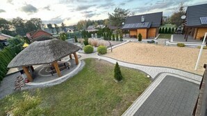 A residential area with a sandy courtyard, a thatched-roof gazebo, and modern houses with solar panels.