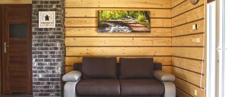 Un interior de madera con una pared de ladrillo, un banco de madera, un reloj y un cuadro con un paisaje.