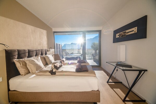 A bedroom with a large bed, a desk, and a view of the outdoors.