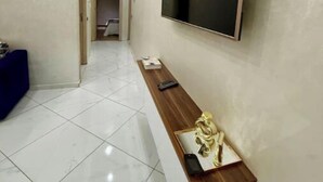 Un couloir moderne avec un téléviseur à écran plat fixé au mur, un banc en bois orné d’une petite statue et un sol carrelé.
