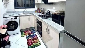 Une cuisine compacte avec des meubles blancs, un four encastré, un four à micro-ondes et un réfrigérateur.
