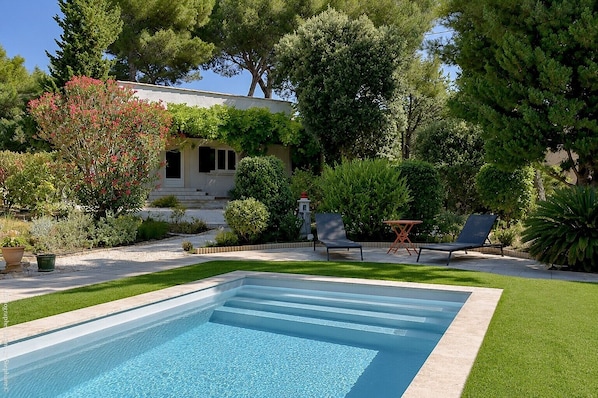 Une piscine dotĂ©e dâune terrasse carrelĂ©e, entourĂ©e de pelouse et de diffĂ©rentes plantes.