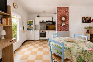 A compact kitchen with white cabinets, a red brick accent wall, a dining table with blue chairs, and a checkered floor. - Country House in Ceyreste (Ceyreste)