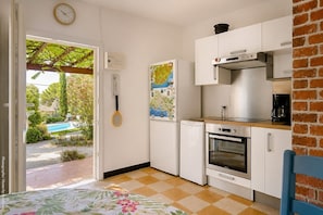 A compact kitchen with white cabinets, a stove, and a coffee maker. There's a map on the wall and a tennis racket hanging.