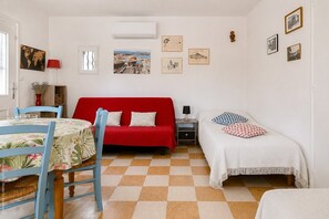 A room with a red sofa, a white bed, a small table with a chair, and a checkered floor. - Country House in Ceyreste (Ceyreste)