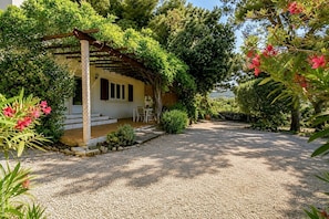 Une maison dotĂ©e dâun porche abritĂ©, dâune allĂ©e en gravier et entourĂ©e de verdure.