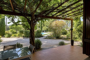 Un espace extĂ©rieur abritĂ©, dotĂ© dâune table et de chaises, entourĂ© dâarbres et bordĂ© dâun chemin de gravier.