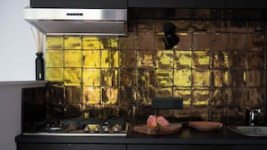 Una cocina con campana de acero inoxidable, salpicadero de azulejos, lámpara empotrada negra, tabla de madera con un objeto rosa y un fregadero.