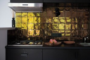 Una cocina con campana de acero inoxidable, salpicadero de azulejos, lámpara empotrada negra, tabla de madera con un objeto rosa y un fregadero.