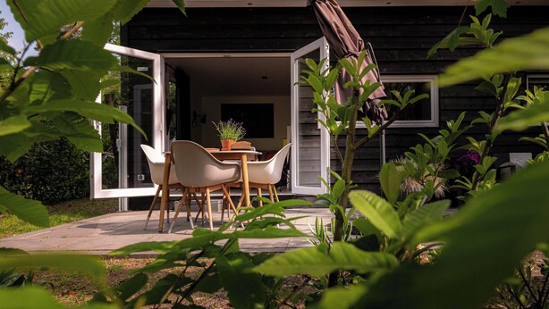 Una casa moderna con un patio amueblado con mesa y sillas, rodeado de follaje.