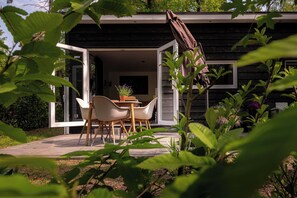 Una casa moderna con un patio amueblado con mesa y sillas, rodeado de follaje.