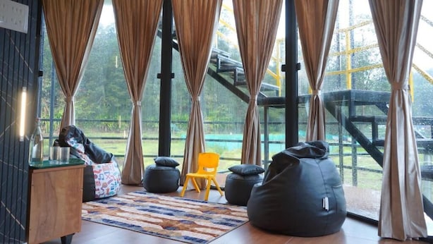 A modern room with large windows, a wooden floor, and a view of a bridge. - Airas Resort (Kodaikanal)