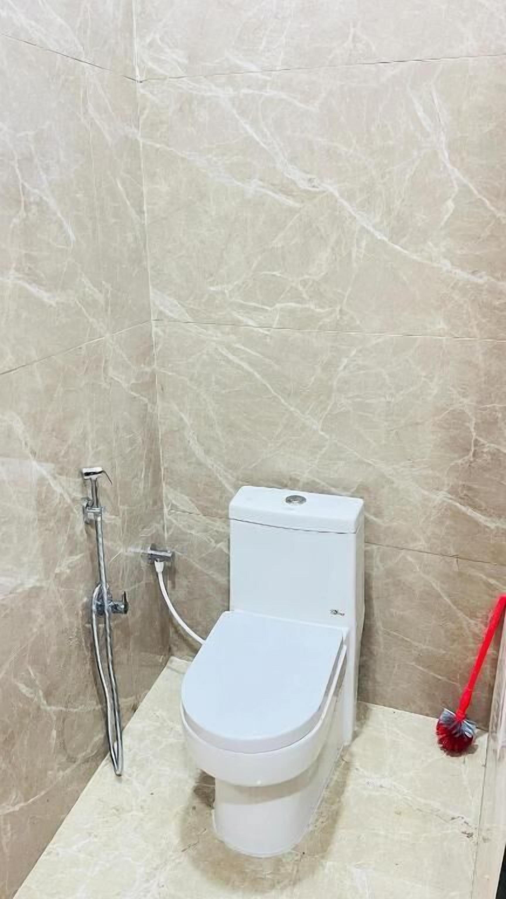 Un baño pequeño con azulejos, un inodoro blanco, una ducha y una herramienta de limpieza roja.