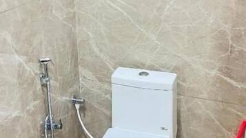 Une petite salle de bain carrelée, avec des toilettes blanches, une douche et un outil de nettoyage rouge.