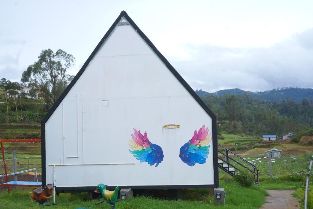Un edificio blanco con techo triangular, pintado con alas de pájaros de colores y un halo.