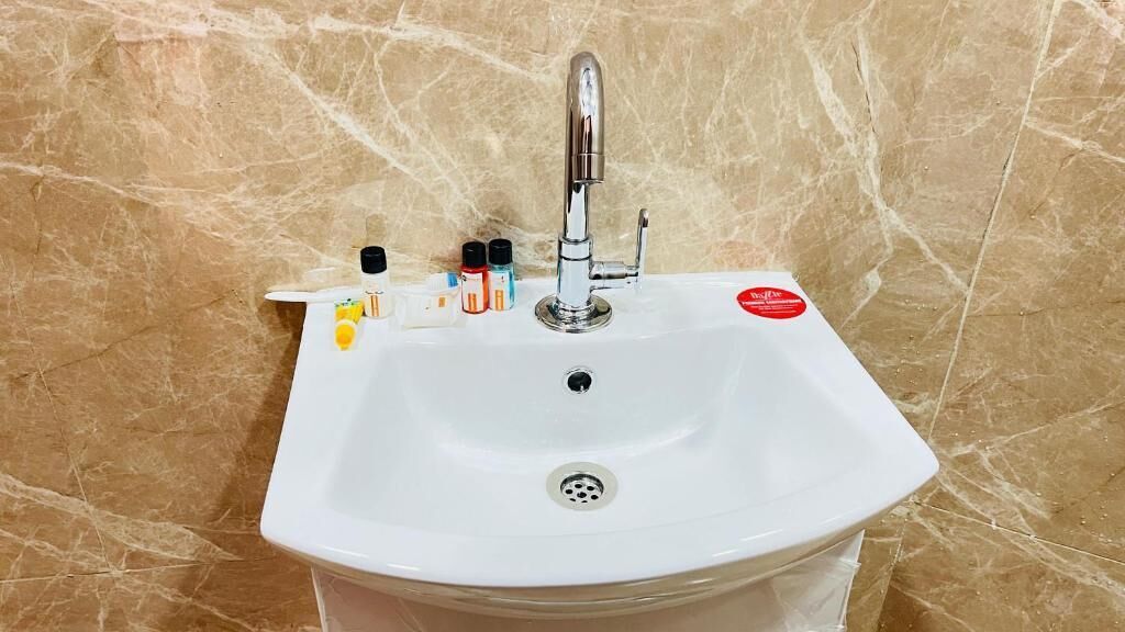 A white bathroom sink with a chrome faucet, a soap dispenser, and a few bottles of soap on the countertop.