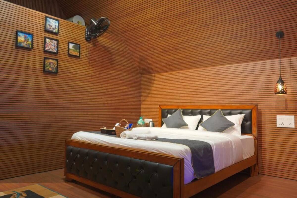 Een net opgemaakt bed met een houten hoofdbord, een wandplank met diverse spullen en een hanglamp.