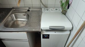 A kitchen with a stainless steel sink, a white washing machine, and a tiled backsplash.