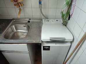 A kitchen with a stainless steel sink, a white washing machine, and a tiled backsplash. - HELLO AND WELCOME. (Rostock)