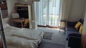 A bedroom with a bed, a desk, a chair, a sofa, a lamp, and a window with curtains.