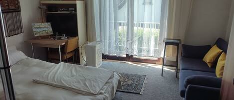A bedroom with a bed, a desk, a chair, a sofa, a lamp, and a window with curtains.