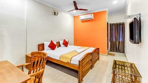A bedroom with a bed, a wooden chair, a small table, an air conditioning unit, a ceiling fan, and a TV mounted on the wall. - Hommetree T Nagar (Chennai)