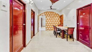 A hotel corridor with red doors, a dining area with a patterned wall, and a ceiling light fixture. - Hommetree T Nagar (Chennai)